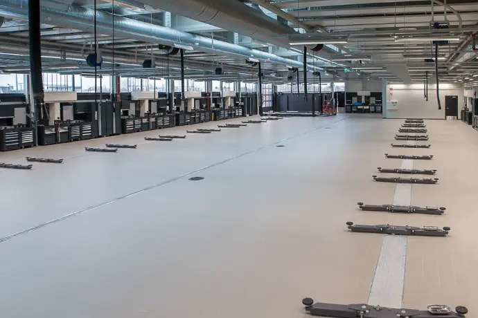 Veho Airport autohuollon uusi korjaamohalli Kuva pitkästä korjaamohallista, jossa lattiaan upotettuja autonostimia rivissä 8 kpl hallin molemmin puolin.