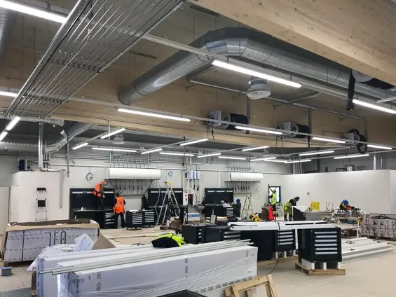 Kuva korjaamon remontointityömaalta, kasattuja kalusteita ja muita laatikoita siellä täällä. 5 työmiestä parhaillaan hommissa eri puolilla korjaamohallia.