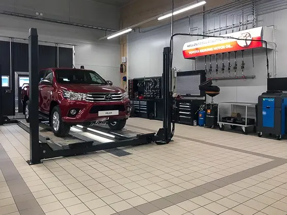 Kuvassa punainen Toyota Hilux nelipilarinostimella, jonka vaalea lattia-alue on kehystetty tummemmilla rajalaatoilla.