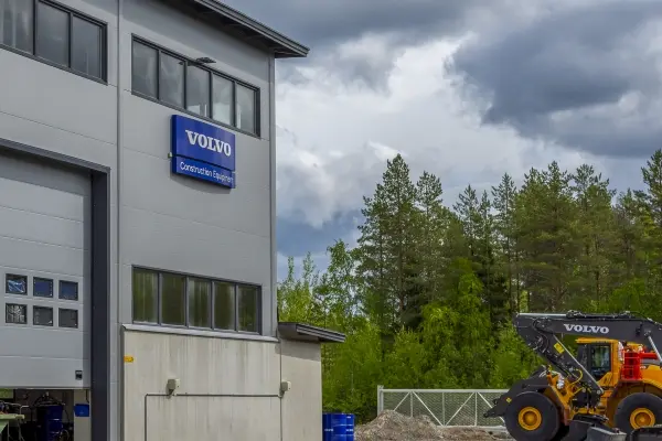Kuva hallista ulkopuolelta. Seinässä kyltti VOLOV Construction Equipment, jonka vieressä suuri nosto-ovi. Pihalla Volvo-merkkinen keltainen työkone.