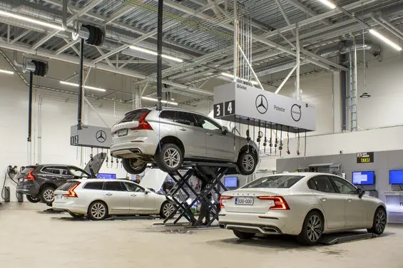 Neljä volvoa autonostimilla rivissä, välissä paineilma ja nestekelastot. Asentajan työpisteet.