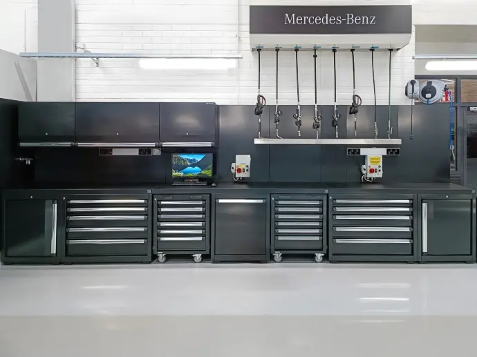 Tummanharmaat D.E.A työkalukaapistot asentajan työpisteellä. Öljy- ja nestekelojen kuoressa tyylikkäästi Mercedes-Benz.