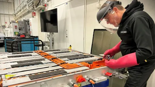 Kuvassa asentaja korjaamassa avointa korkeajänniteakkua jännitetyövarusteet, hanskat ja visiiri päällä.